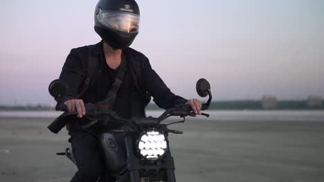 concentrated biker rides on black sport bike in helmet with switched front headlight. evening dusk