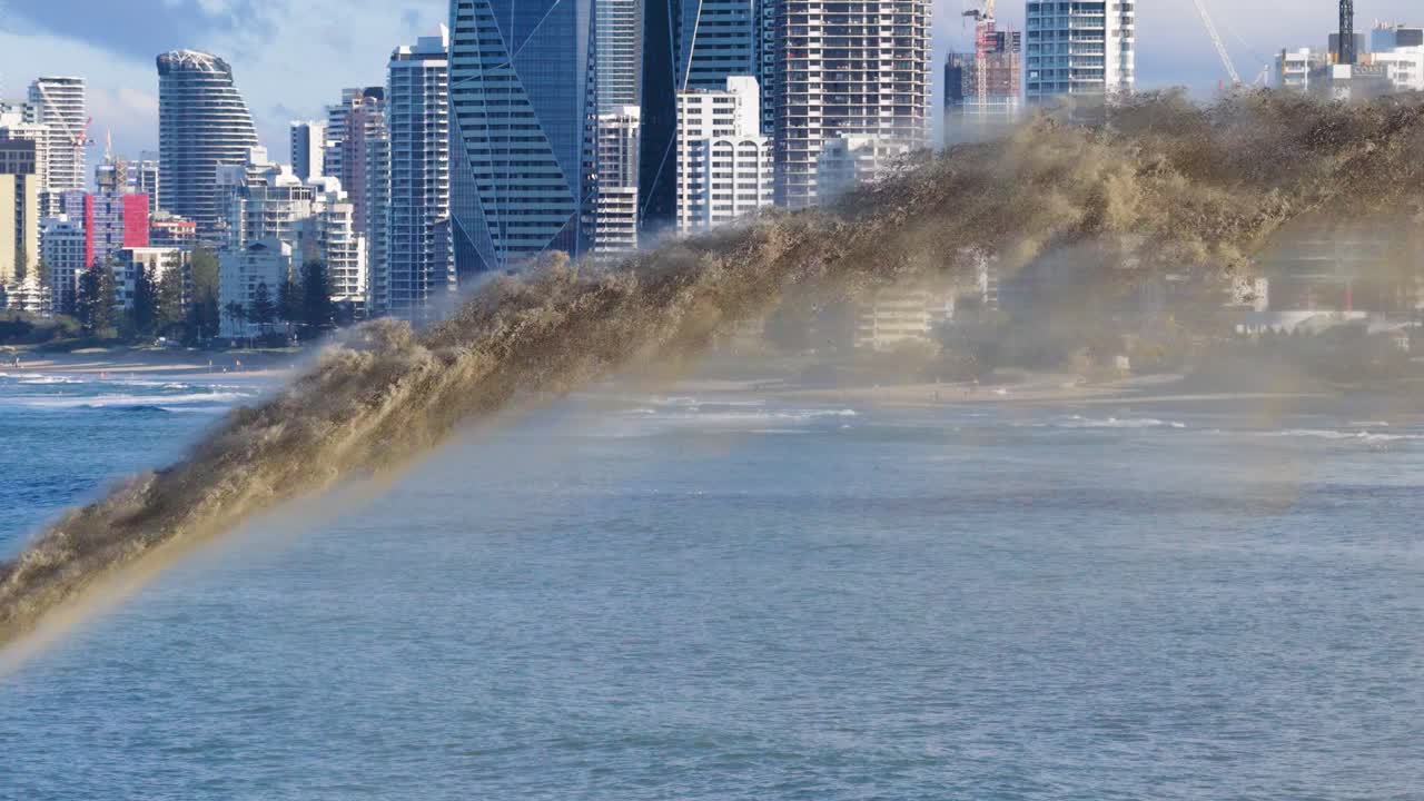 Sand is pumped into the ocean near a city skyline, illustrating coastal erosion management under clear skies