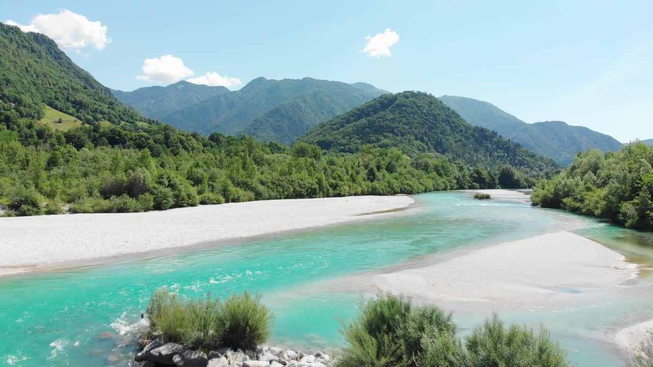 드론은 유럽 슬로베니아의 화창한 여름날 푸른 언덕을 배경으로 조약돌 해변과 청록색 맑은 산 강 위로 날아갑니다.