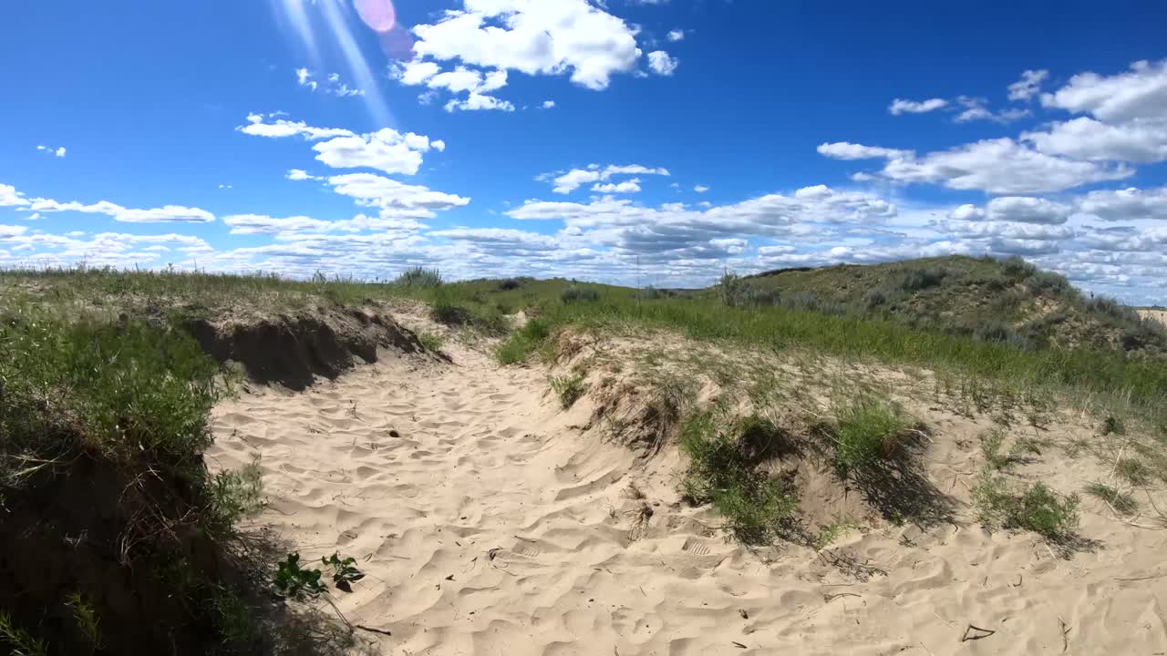 un sendero hecho de arena que se aleja en el campo en un día nublado y soleado