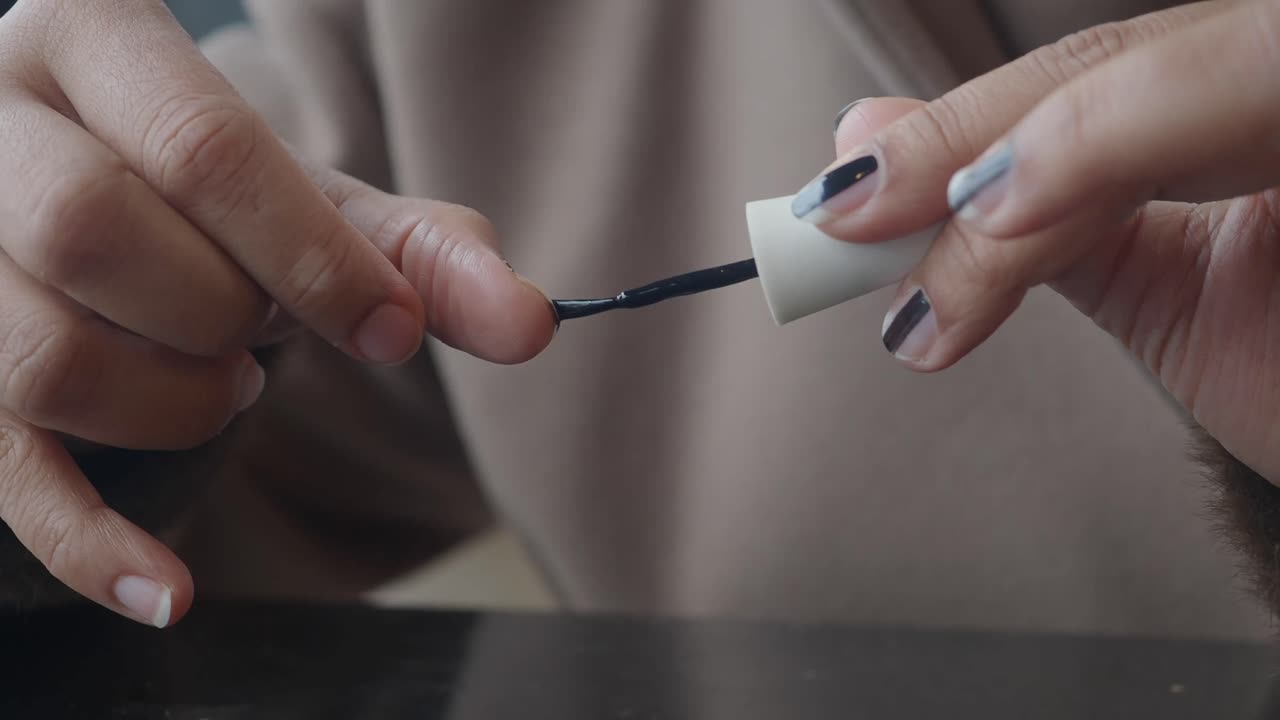 Nærbillede af en person, der påfører mørk neglelak på en fingernegl