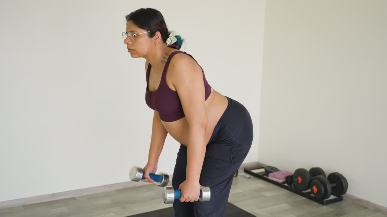 Donna indiana incinta che allena le spalle con i pesi durante il terzo trimestre di gravidanza