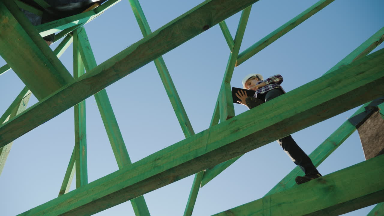 미완성 지붕의 서까래 사이에서 태블릿으로 작업하는 여성 건축업자