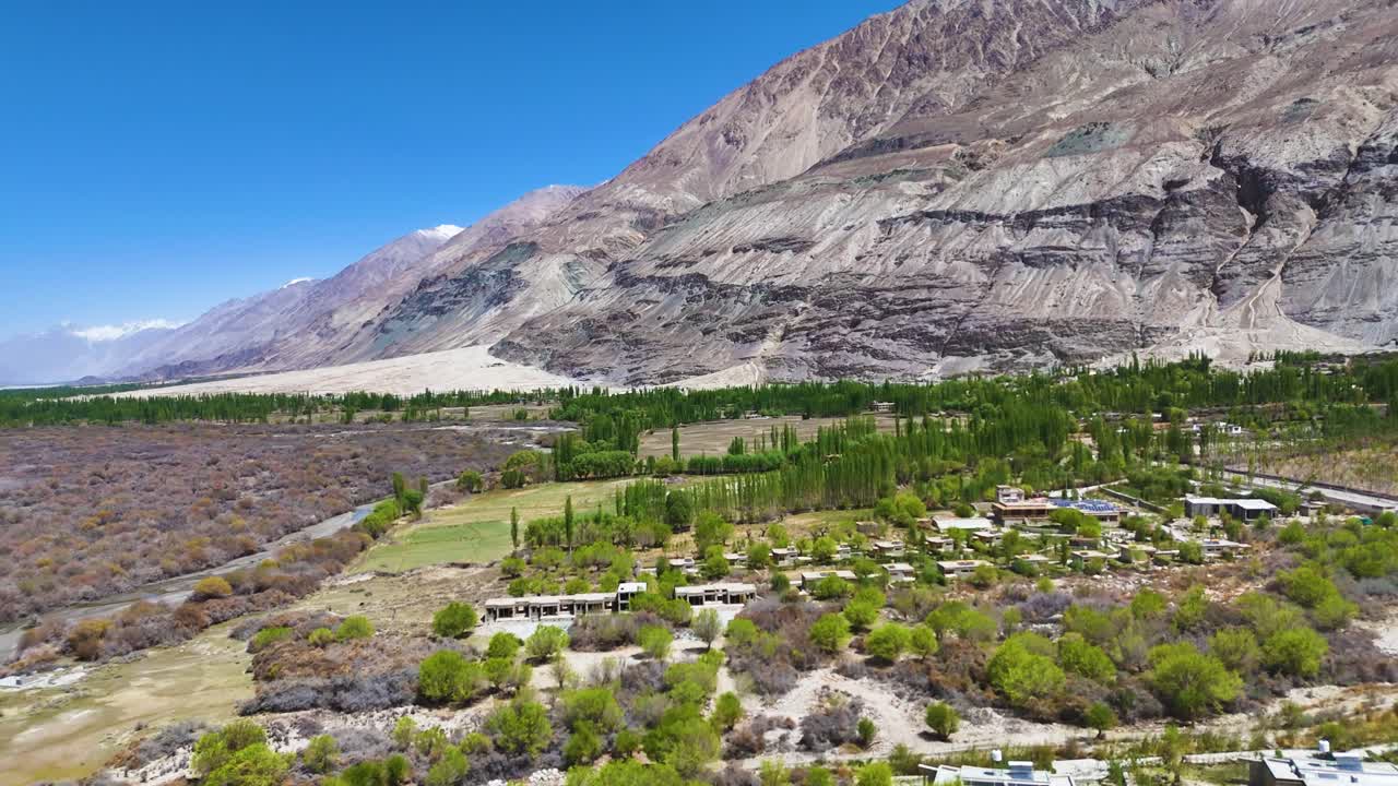 Aerial drone shot capturing a car driving across a vast, empty Ladakhi plateau under a deep blue sky.