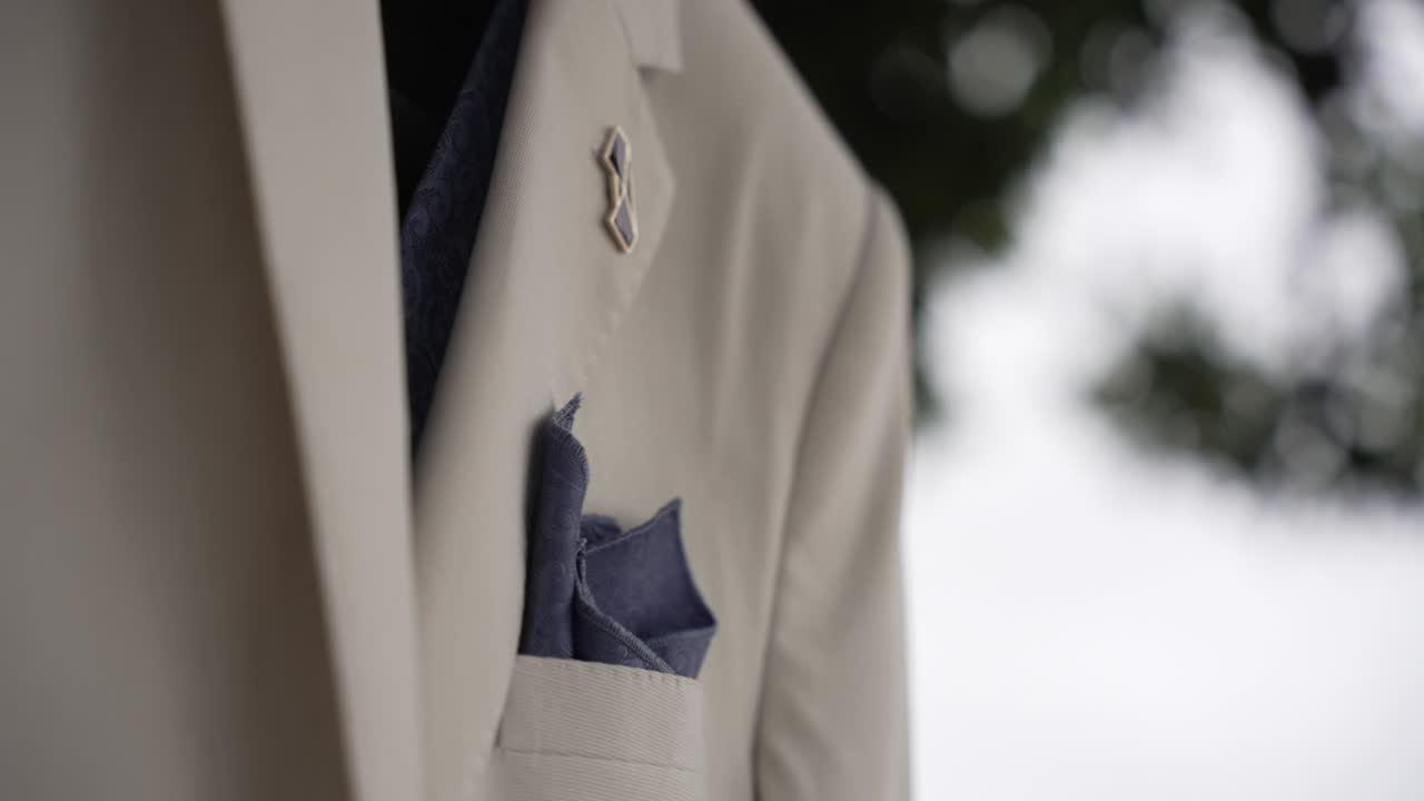 un primer plano de un traje de boda beige con un detalle cuadrado de bolsillo azul.