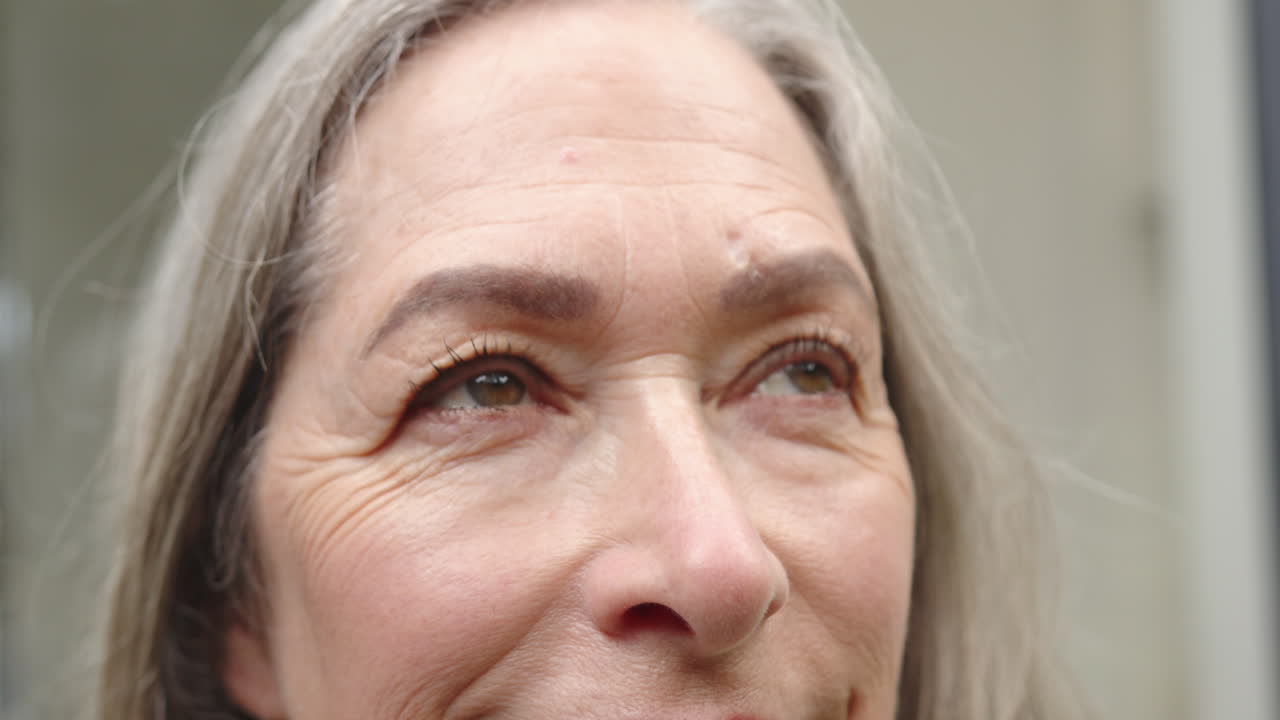 Smiling woman with gray hair looking up, showing facial expressions and wrinkles, at home