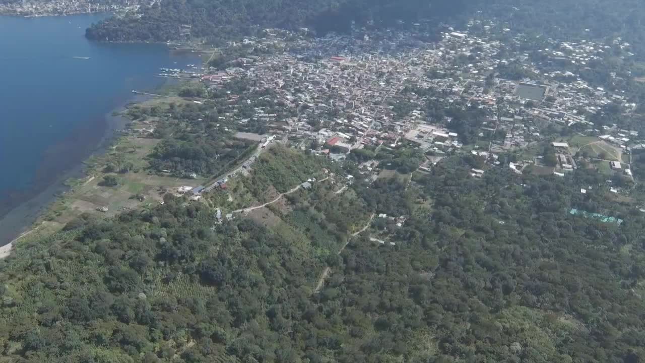 산 후안 라 라구나 (san juan de la laguna) 의 넓은 공중 풍경, 아티트란 호수, 울창한 초록색, 농경지 및 밀집된 도시 건물을 보여줍니다.