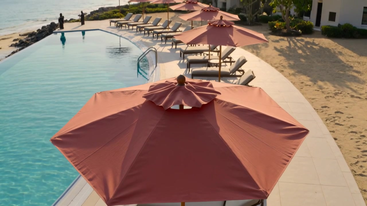 Drone che si allontana rivelando un grande ombrellone rosso a bordo piscina su un ponte pavimentato, mostrando una persona seduta