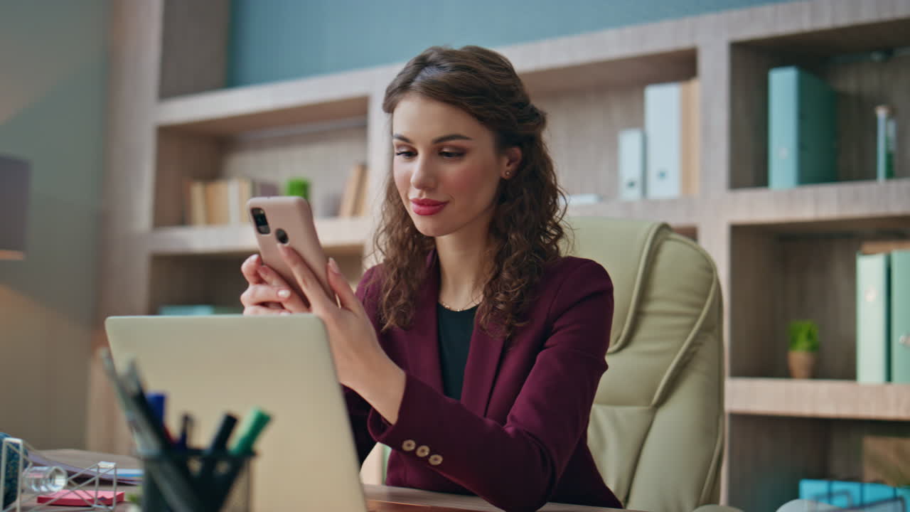 Laughing employee receiving message in smartphone. Happy woman working laptop