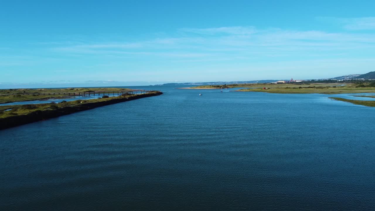 Low Pushing Aerial on Beautiful Estuary with Calm Blue Water Leading Out to Sea at High Tide with Lone Boat with Low Lying Wetlands and Swansea City in Distance