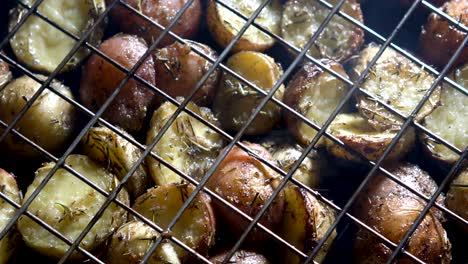 camera looking straight down at browned herbed new potatoes in a wire basket on a hot grill with red embers glowing beneath