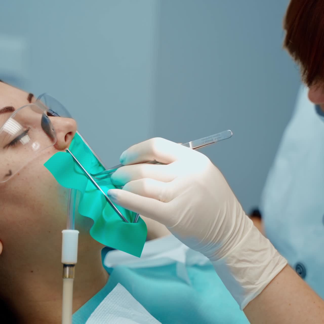 Face of a patient in protective glasses in the dental chair. Professional stomatologist treating woman's teeth in dental center. Stomatology concept.