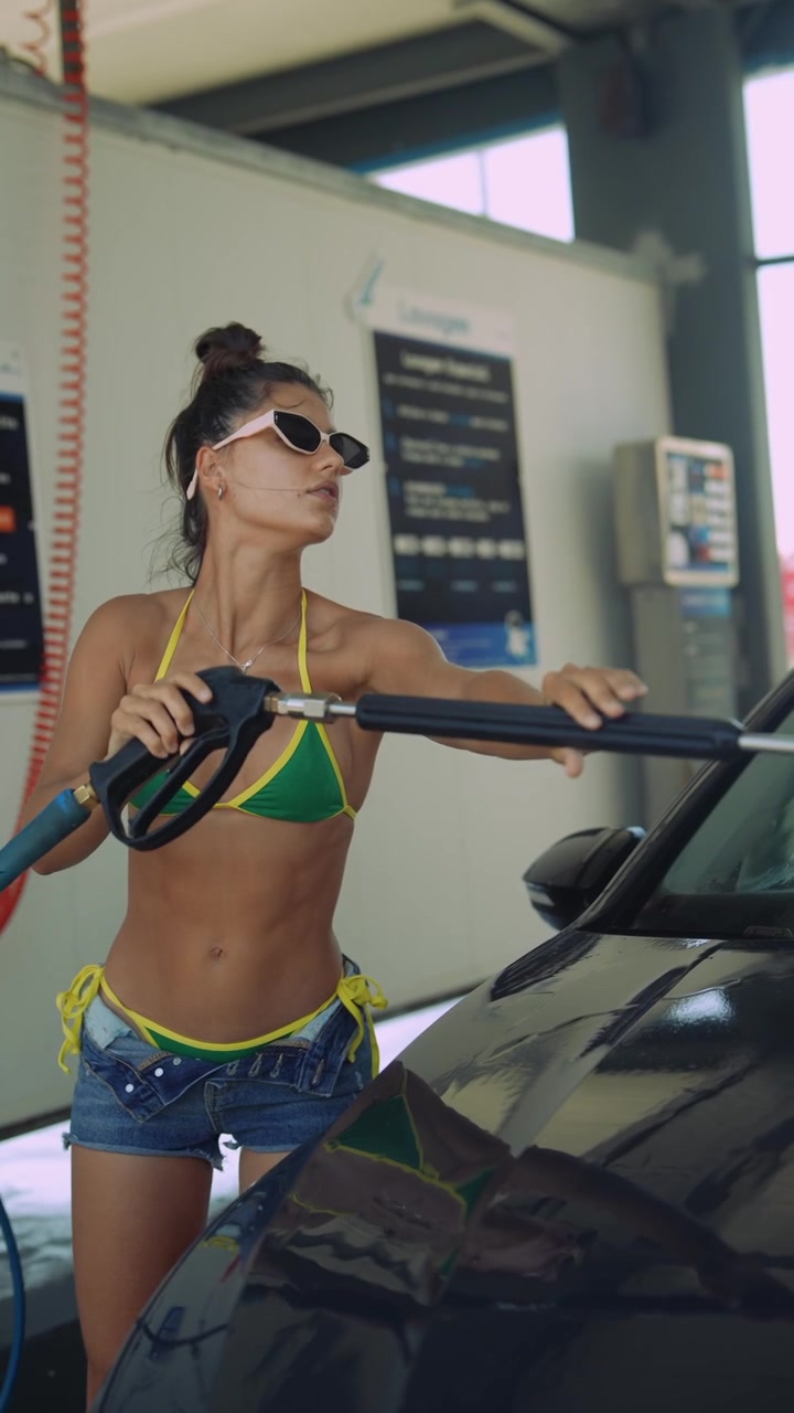 Junge Frau im Bikini wäscht Auto in der SB-Waschanlage