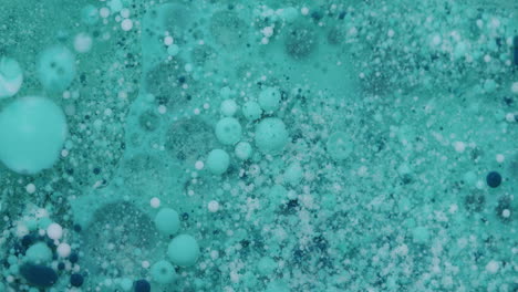 macro shot of small turquoise, white and blue bubbles moving in a transparent liquid