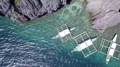 4k top down aerial drone view of banca outrigger boats at miniloc island in philippines in beautiful blue tropical water