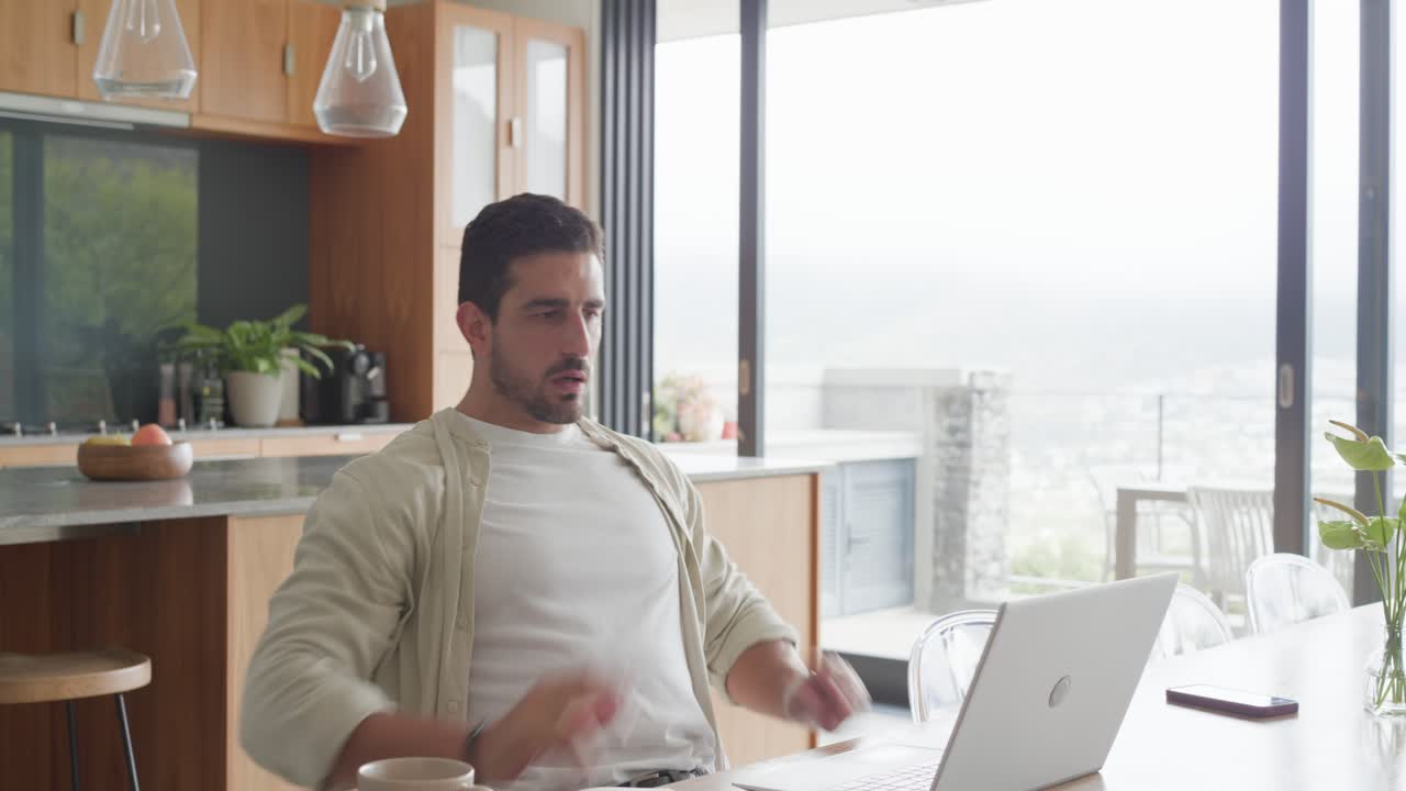 Homem de camisa aberta iniciando sessão no laptop à mesa da cozinha, digitando, alongando-se, finalizando relatório