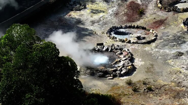 Vista aerea delle fumarole di Furnas dove il vapore sale da bocche geotermiche, circondate da rocce scure e texture vulcaniche contrastanti nelle Azzorre, Portogallo.