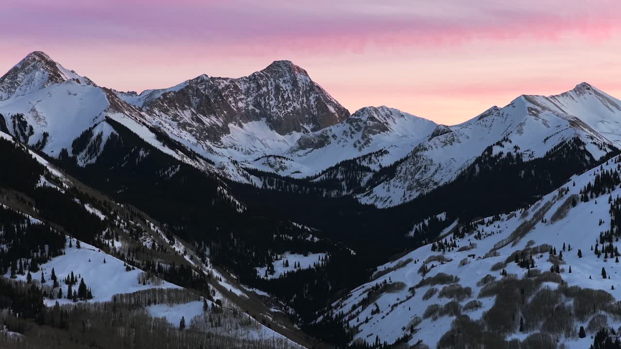 Tramonto invernale vibrante nella Capitol Peak Wilderness, paesaggio naturale panoramico ripreso con drone aereo nel Colorado. Si vedono la valle di Aspen Snowmass, le Elk Range alle ultime luci, le Montagne Rocciose, Longs Peak e Maroon Bells, con una panoramica in avanti verso l'alto.