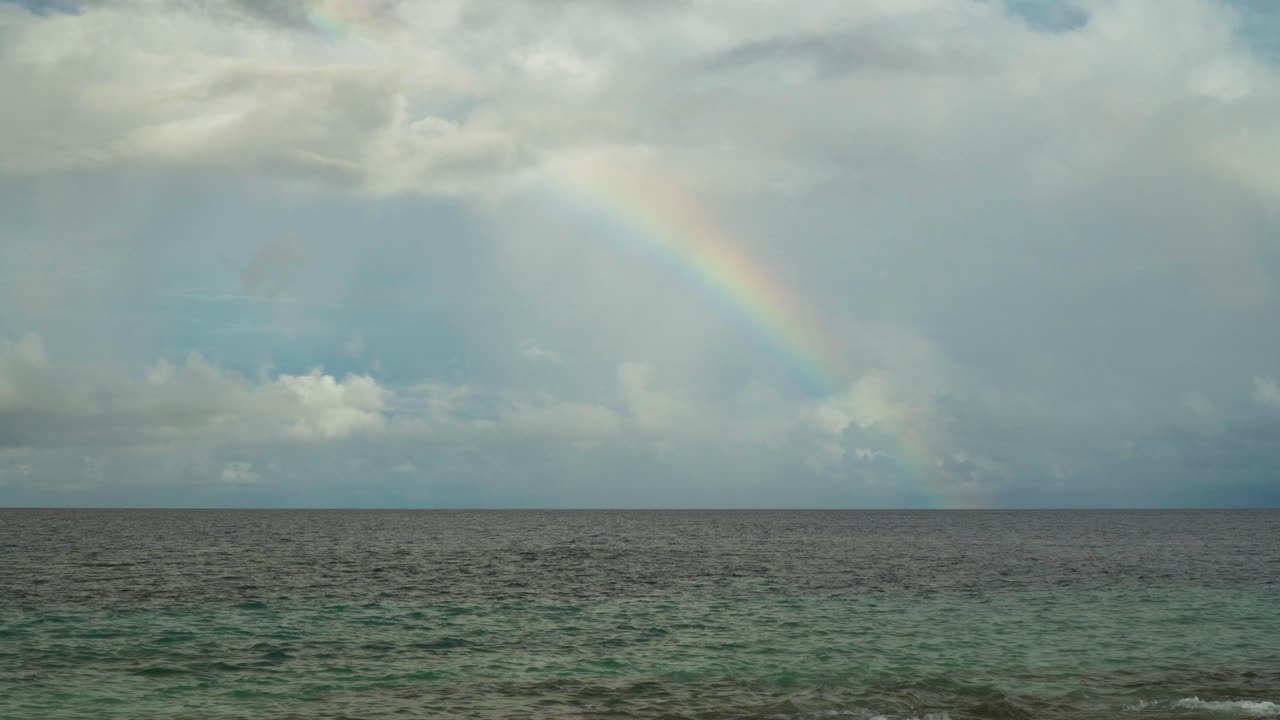 cuarto colorido de un arco iris aparece sobre el océano con nubes de lluvia detrás de él