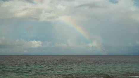 cuarto colorido de un arco iris aparece sobre el océano con nubes de lluvia detrás de él