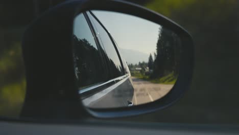 Reflection-in-the-side-mirror-of-a-car-driving-in-Alberta-in-Canada,-with-mountains-in-the-background