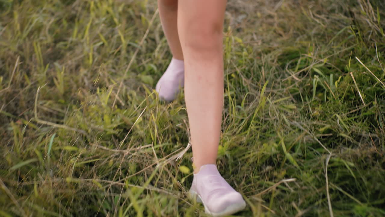 Close-up of legs walking on grassy field in soft pink shoes, capturing motion and texture of dried grass, slow, relaxed steps create a peaceful outdoor vibe
