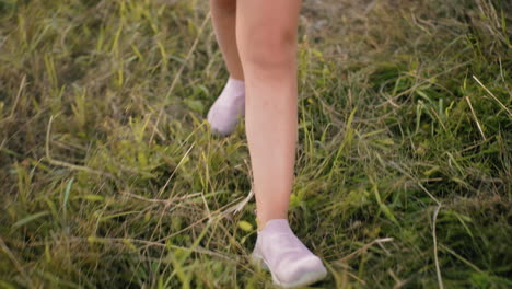 close-up of legs walking on grassy field in soft pink shoes, capturing motion and texture of dried grass, slow, relaxed steps create a peaceful outdoor vibe