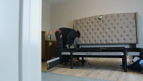 reveal shot of delivery worker assembling electronic motion base bed frame and headboard in customer bedroom