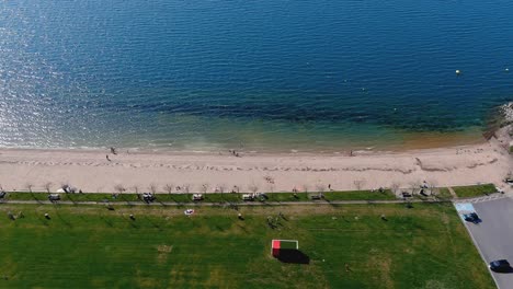 playa del lago con gente tomando el sol y bañándose, jardín y zona de paseo