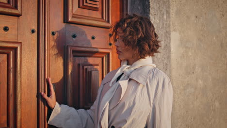 elegant woman posing wooden door at evening sunlight closeup. curly-haired lady