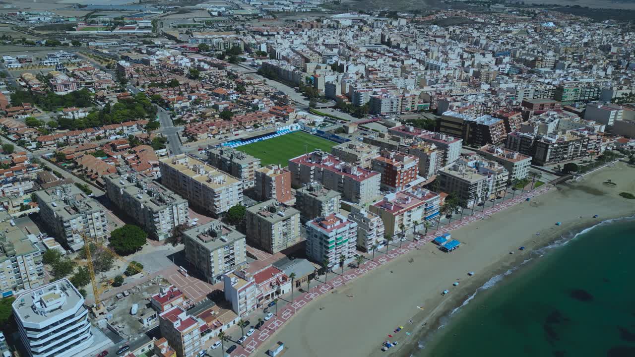 Aerial view of Águilas in the Murcia region of Spain, showcasing Estadio El Rubial beside the beachfront, surrounded by dense urban housing and the Mediterranean coastline