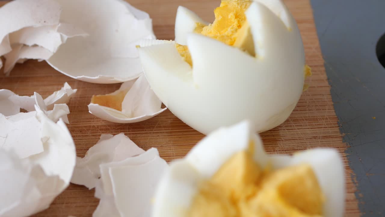 Close up of two peeled hard boiled eggs on a cutting board with shell pieces