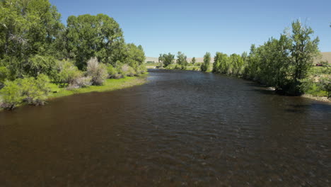 drone flies over countryside shallow river, rises to reveal mountain