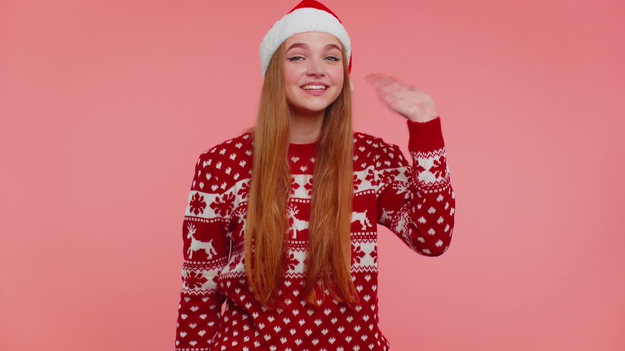 mujer en suéter de navidad agita la palma de la mano en el gesto de saludo da la bienvenida a alguien para celebrar el año nuevo