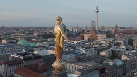 AERIAL:-Golden-Statue-Close-up-on-Church-Cathedral-Rooftop-in-Berlin,-Germany-with-Alexanderplatz-TV-Tower-in-Background-at-Dusk