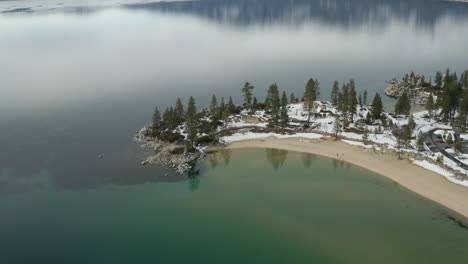 Aerial-descent-over-a-winter-Sand-Harbor-Beach-in-Lake-Tahoe-Nevada-with-snowfall-up-to-the-water-line