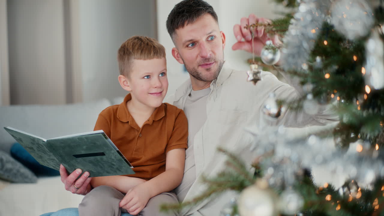 작은 소년은 아빠가 크리스마스 트리를 장식하고 크리스마스 장식으로 장식하는 데 도움을 줍니다.