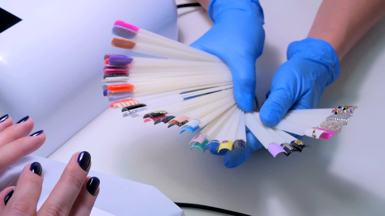 el técnico de uñas muestra la paleta de colores de los servicios de uñas en el salón de belleza.