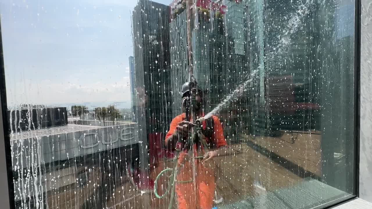 Window cleaner hanging on a rope abseiling on a high rise office building in Singapore