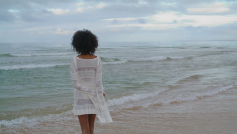 woman contemplating ocean beach vertically shot. curly slim girl looking sea