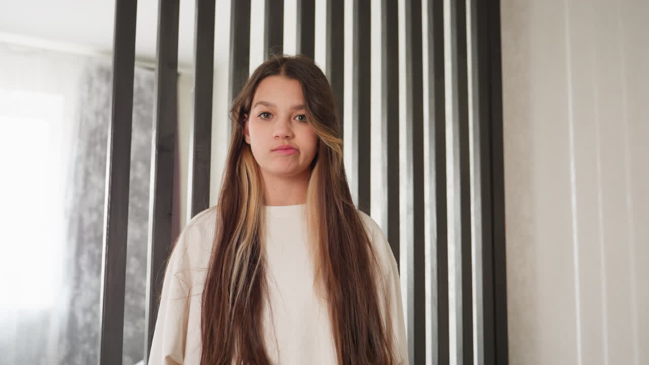 Portrait of young lady standing before wooden divider, long hair frames face, playful pout, neutral pose, soft daylight, interior, vertical slats behind, calm mood, expression captured mid glance