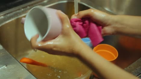 washing cups and dirty knife over sink. handheld shot. close up.