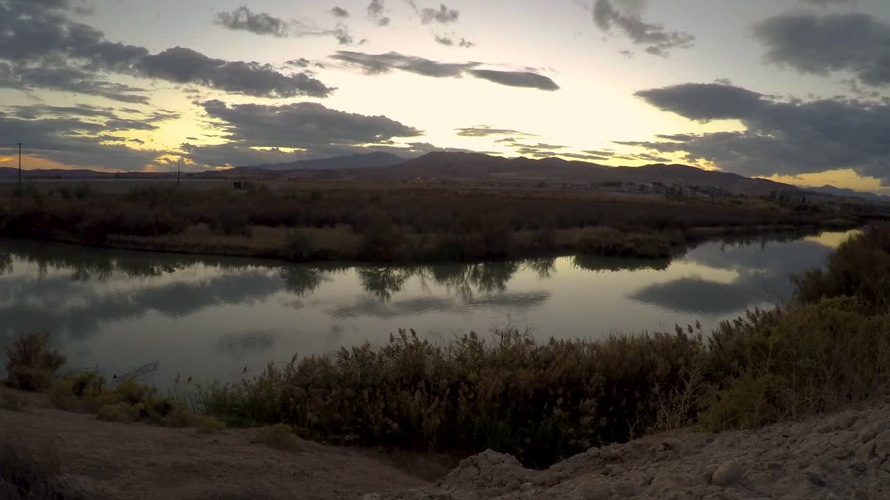 lapso de tiempo estático de un paisaje de nubes al atardecer que se refleja en la superficie lisa de un río con montañas en el fondo