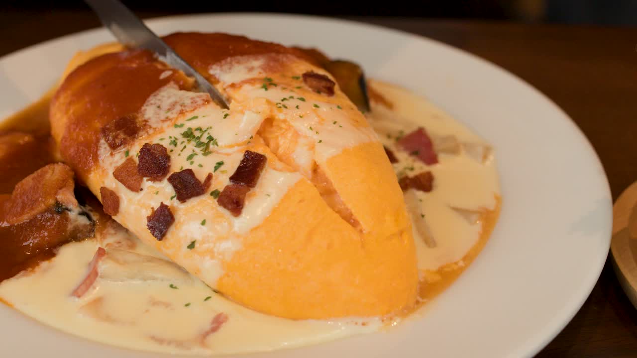 Knife slices omelette rice, creamy sauce spreads, salad bowl beside, warm restaurant lighting, static shot