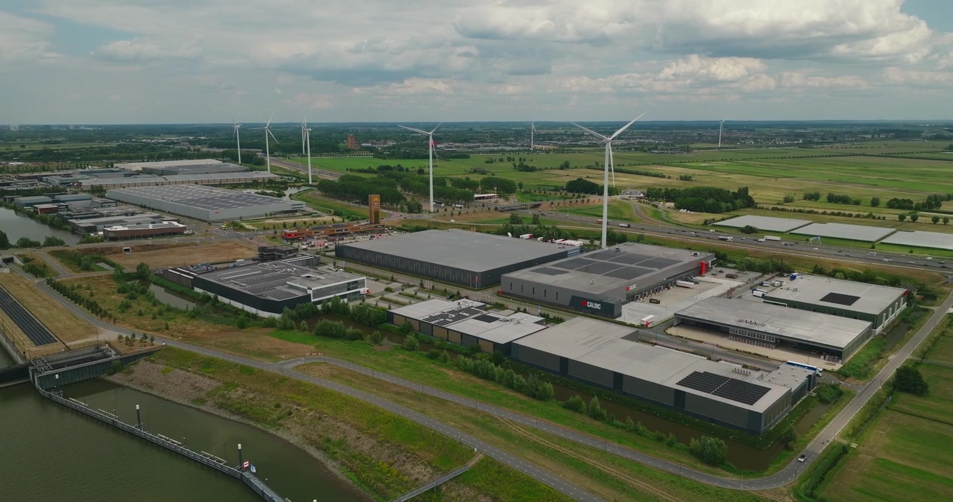 Aerial drone orbit around a modern business park bordering a river, with windmills in the distance and a flat Dutch polder countryside landscape. Commercial Zone