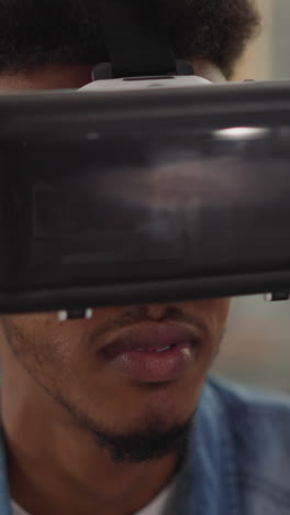 bearded african-american guy with vr headset enjoys 3d movie effects sitting with friends in living room closeup slow motion. technology of entertainment