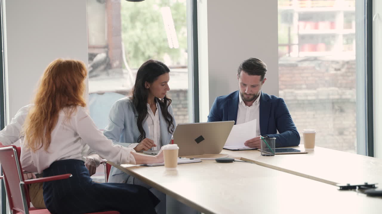 Business meeting between two women and two businessmen. One of the parts hands over a contract to sign and the other part does it.