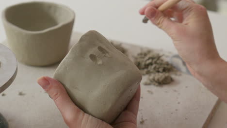 masterfully crafting intricate designs into soft clay with a specialized tool, showcasing artisan's delicate touch