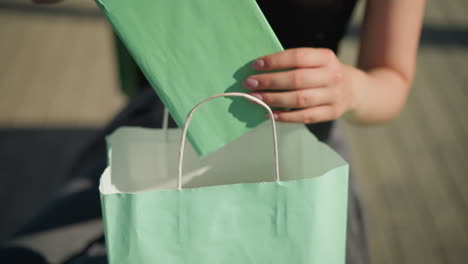 close-up of a lady's hands searching through a mint green shopping bag and retrieving a mint color book, the background shows her slightly blurred while she continues her search