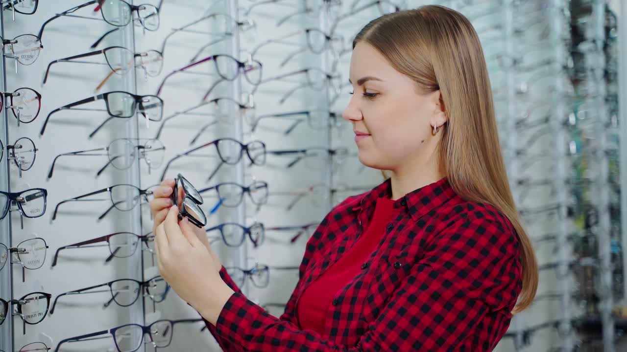 Female customer in the optical store. Beautiful young woman choosing new stylish eyeglasses in the shop. Eyewear concept.